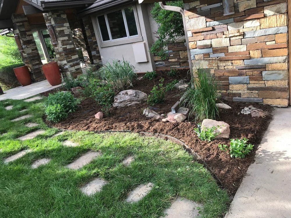 Modern landscaped garden with stone accents, mulch, and lush green plants around a home.
