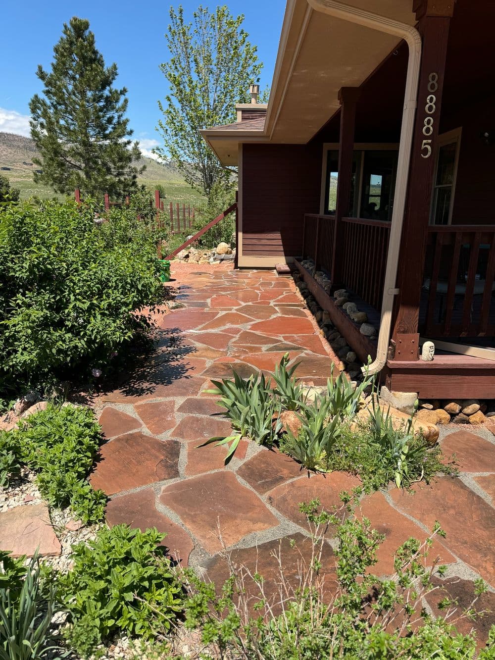 Stone pathway leading to a house, bordered by greenery and mountain views on a sunny day.