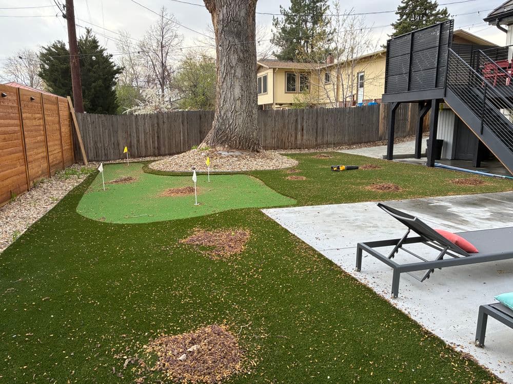 Backyard putting green with flags, surrounded by artificial grass and a patio area.